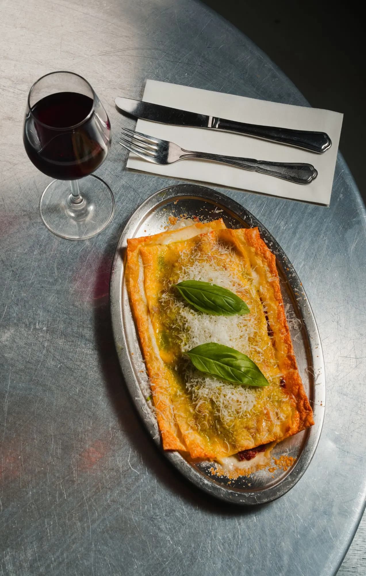 2 sheet lasagne with parmigiano and basil on a steel plate, with a glass of red wine